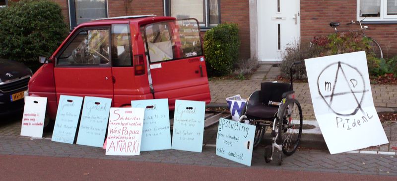 Foto van een rode Canta en rolstoel, met daarvoor 8 protestborden.